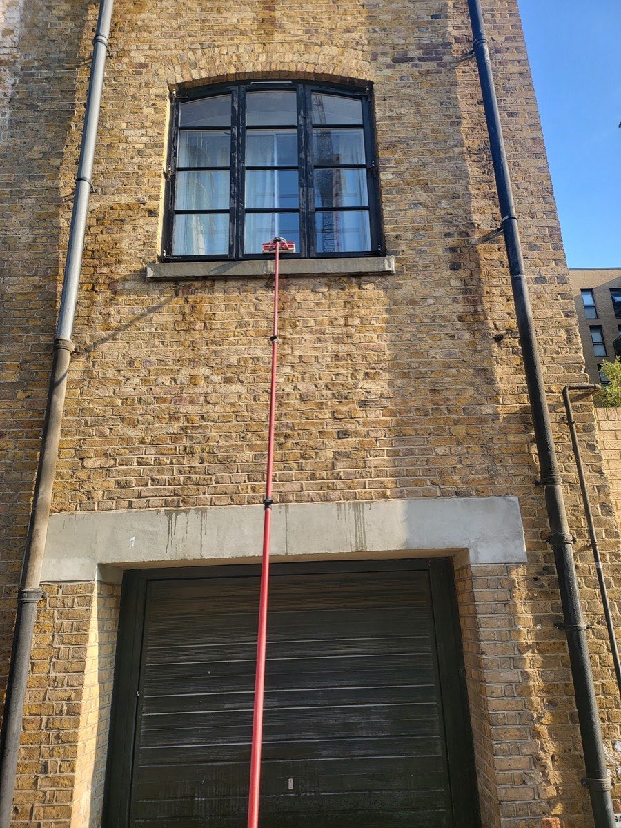 Reach-and-wash pole cleaning an arched warehouse window in East London